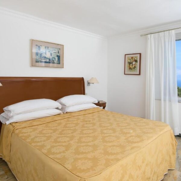 Chambre de l'Hôtel Bellavista à Anacapri avec lit double, couvre-lit jaune et fenêtre vue mer.
