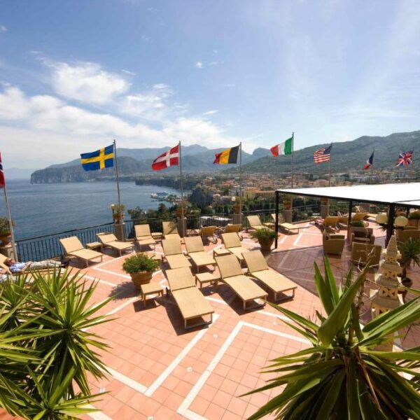 Solarium de l’Hotel Bristol à Sorrente avec transats, drapeaux et panorama sur la côte.