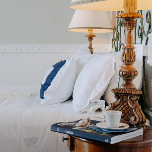 Intérieur raffiné d'une chambre à l'Hôtel Caesar Augustus avec lit blanc et table de chevet ancienne.