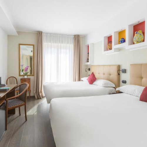 Chambre de l’Hotel Central à Sorrente avec deux lits, décoration claire et touches colorées.