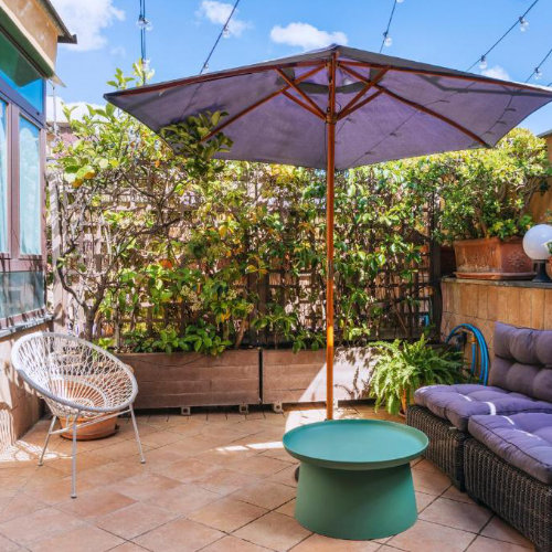 Terrasse fleurie et ensoleillée de l'Hôtel Convento avec mobilier de jardin moderne et parasol.