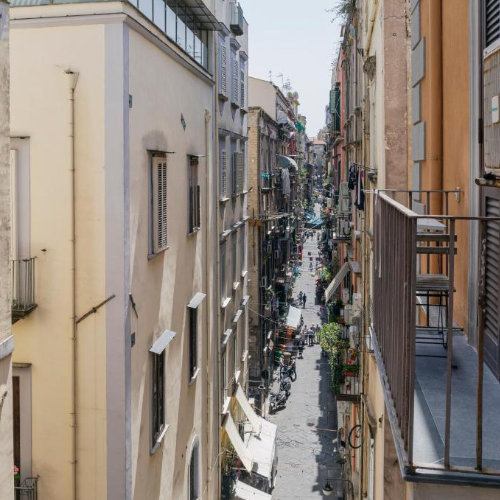 Vue plongeante sur une ruelle étroite et animée de Naples bordée de bâtiments historiques aux façades typiques.