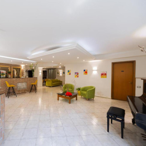 Hall de l'Hôtel Dalì avec piano, bar en briques et fauteuils verts.