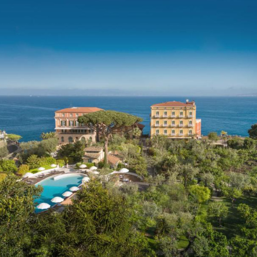 Vue de l’Hotel Excelsior Vittoria à Sorrente avec jardins, piscine et mer en arrière-plan.