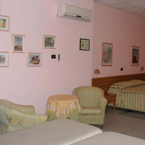 Chambre spacieuse aux murs roses avec un coin salon composé de fauteuils vert clair et un lit double au fond.