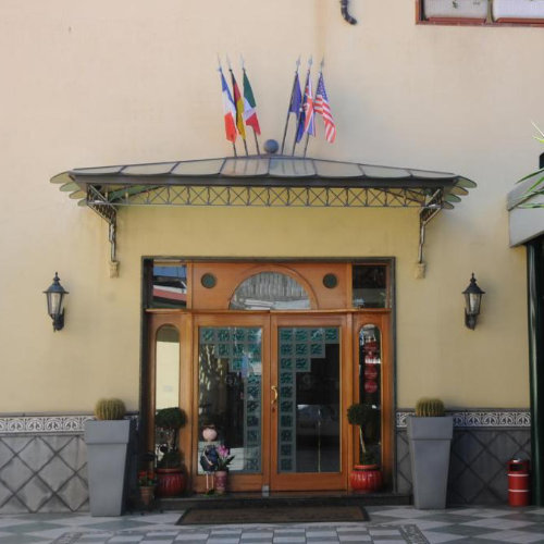 Entrée élégante d'un hôtel avec une porte en bois vitrée, surmontée d'un auvent en verre et de plusieurs drapeaux nationaux.