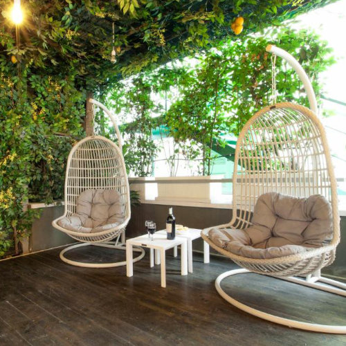 Espace de détente sur une terrasse décorée de feuillage avec deux fauteuils suspendus blancs et une petite table basse.