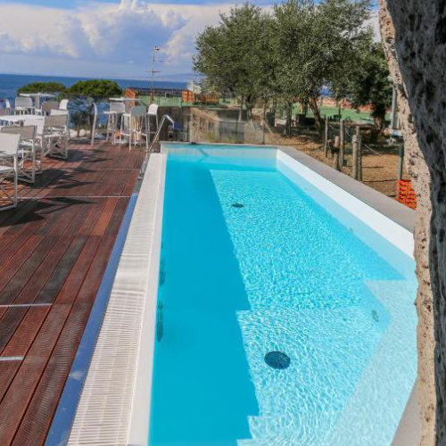 Piscine de l’Hotel Il Faro à Sorrente avec terrasse, oliviers et vue sur la mer.