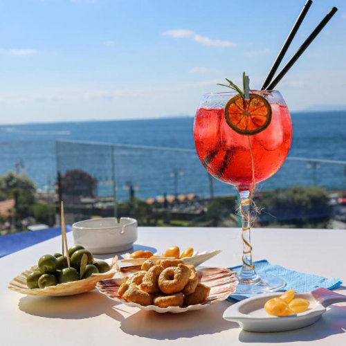 Cocktail en terrasse à l’Hotel Il Faro à Sorrente avec apéritif et panorama marin.