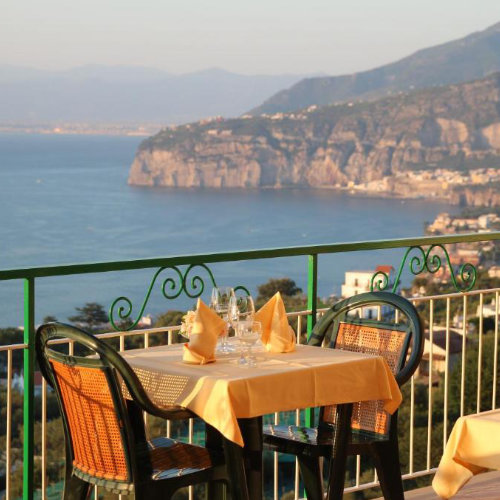 Terrasse de restaurant avec tables dressées et vue sur la baie de Sorrente.