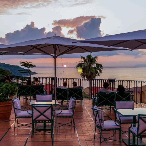 Terrasse de l’Hôtel Bristol à Sorrente avec fauteuils, grandes ombrelles et vue sur la mer au coucher du soleil.