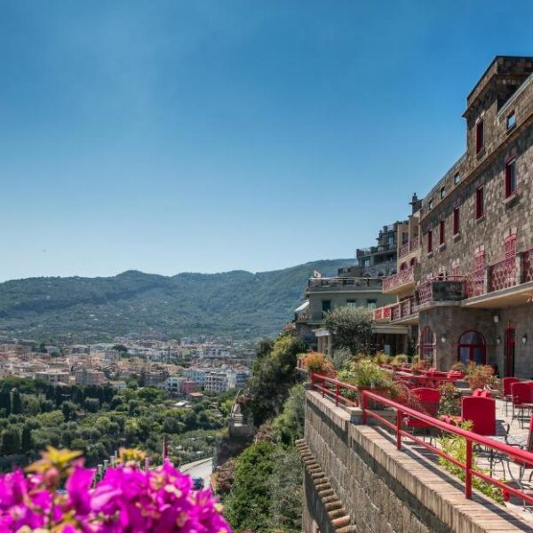 Vue panoramique depuis l’Hotel Minerva à Sorrente avec terrasse, tables rouges et mer bleue.