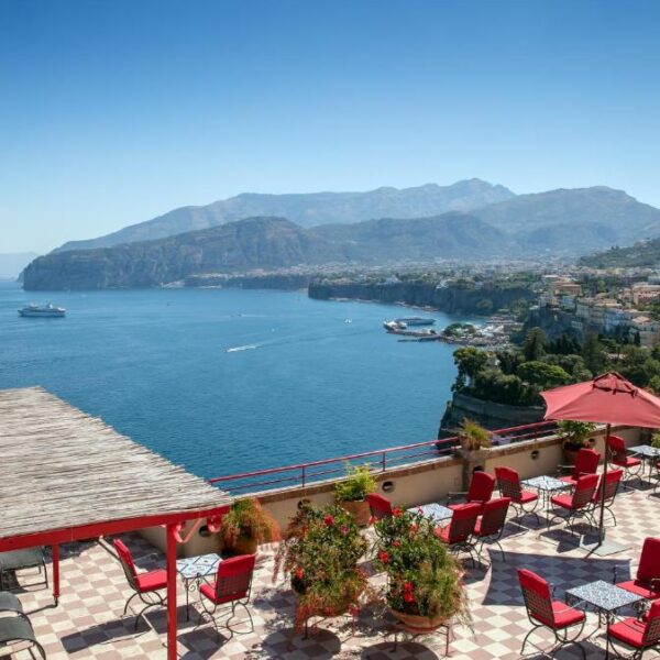 Terrasse panoramique de l’Hotel Minerva à Sorrente avec chaises rouges, parasol et vue sur les collines.