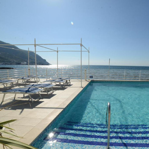 Vue de l'extérieur de l'hôtel moderne avec sa piscine en terrasse dominant la plage et les montagnes environnantes.