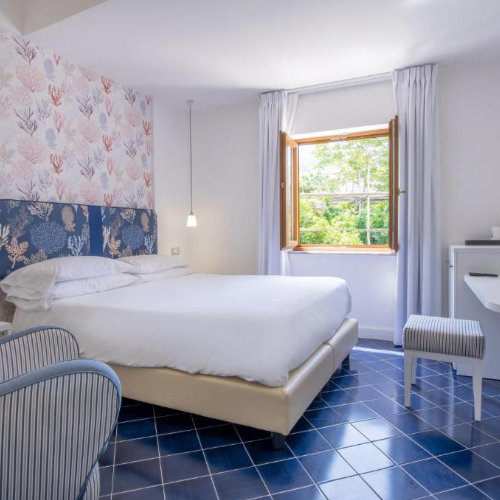 Chambre de l’Hotel Nice à Sorrente avec lit double, carrelage bleu et décoration moderne.