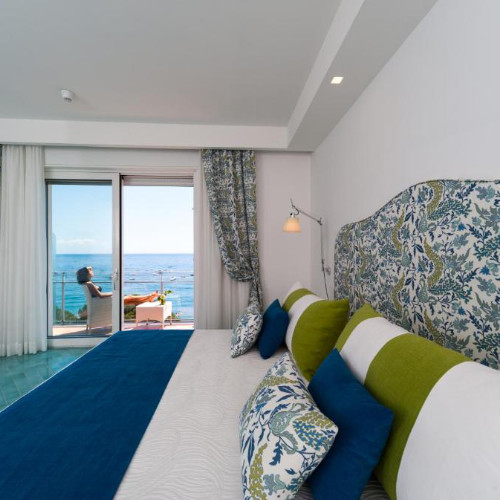 Chambre lumineuse avec lit aux tons bleu et vert et balcon offrant une vue sur la mer.