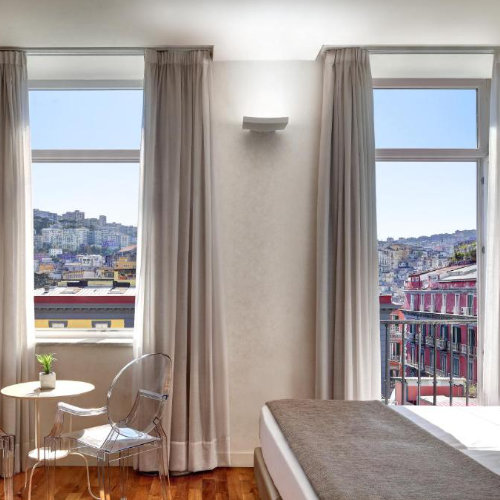 Chambre lumineuse de l’Hotel Piazza Bellini à Naples avec vue sur le centre historique.
