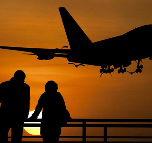 Avion en phase d’atterrissage au coucher du soleil avec silhouettes de voyageurs observant depuis un belvédère à Naples.