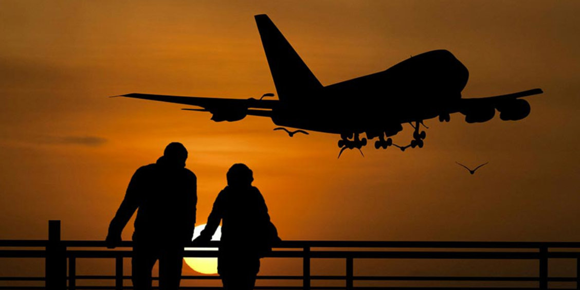 Avion en phase d’atterrissage au coucher du soleil avec silhouettes de voyageurs observant depuis un belvédère à Naples.