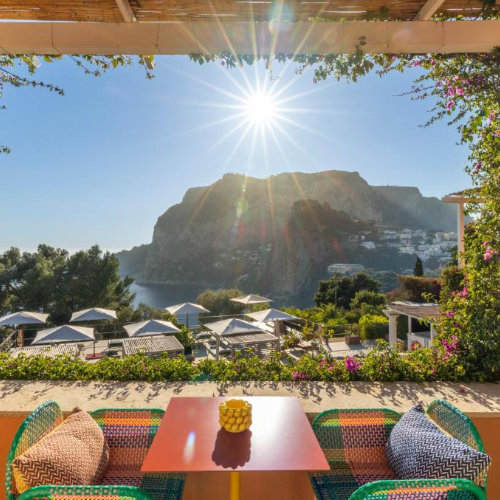 Terrasse ensoleillée de l'hôtel Punta Tragara à Capri avec table colorée et vue sur le paysage côtier.