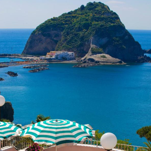 Vue du rocher de Sant'Angelo depuis la terrasse de l'hôtel avec ses parasols rayés.