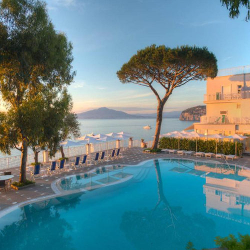 Piscine de l’Hotel Riviera à Sorrente avec pin parasol, transats et vue sur le Vésuve.