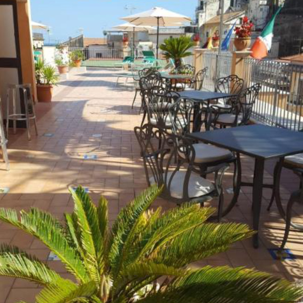 Terrasse ensoleillée de l'Hôtel Santa Lucia avec tables, chaises et parasols.