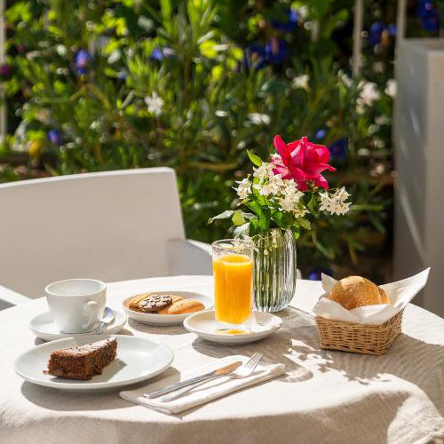 Petit-déjeuner en terrasse à l'Hôtel Senaria avec jus d'orange, pâtisseries et fleurs fraîches.