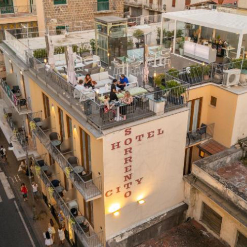 Vue extérieure du bâtiment de l'Hôtel Sorrento City montrant sa façade avec des balcons et son toit-terrasse animé où des clients sont installés.