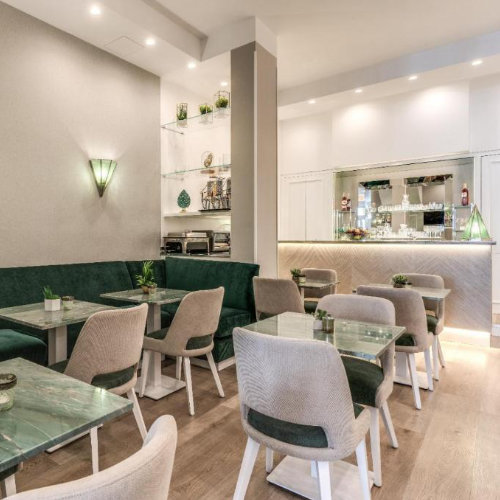 Intérieur chic du restaurant de l'hôtel avec des banquettes en velours vert, des chaises contemporaines et un bar élégant au fond.