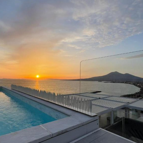 Piscine à débordement sur un toit-terrasse au coucher du soleil, offrant une vue sur la mer et la silhouette du mont Vésuve.