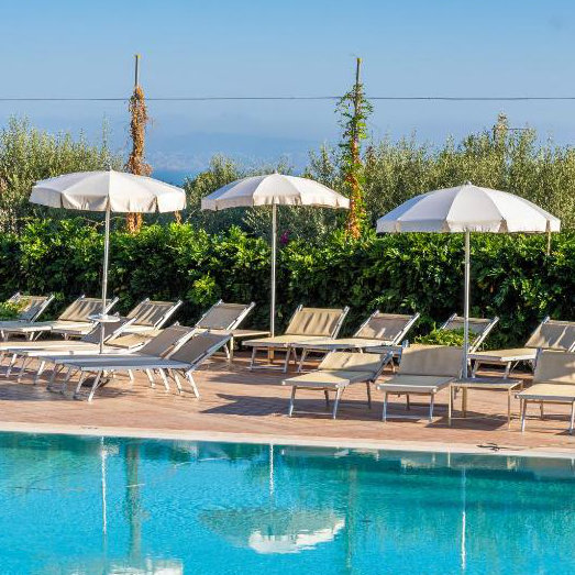 Piscine de l’Hotel Vesuvio à Sorrente avec transats, parasols blancs et jardin.
