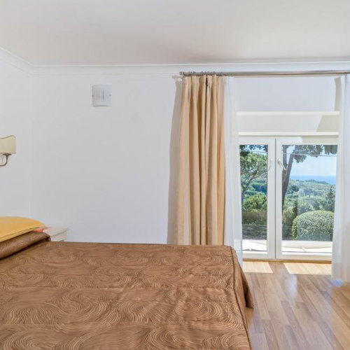 Chambre lumineuse de l'Hôtel Villa Ceselle à Capri avec vue sur les collines et la mer depuis le balcon.