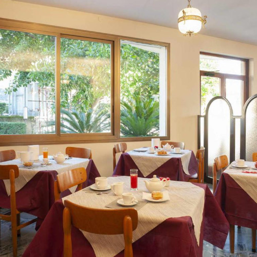 Salle de petit-déjeuner de l'hôtel avec des tables dressées devant de grandes baies vitrées donnant sur la végétation.