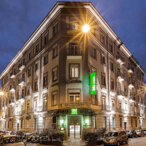 Façade illuminée du bâtiment historique de l'hôtel Ibis Styles Naples Garibaldi à la tombée de la nuit.