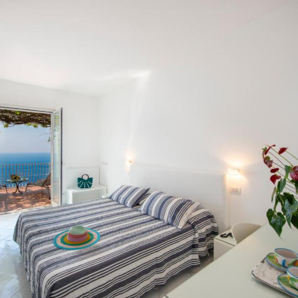 Chambre lumineuse de l’Hotel Il Barilotto à Positano avec accès à la terrasse vue mer.