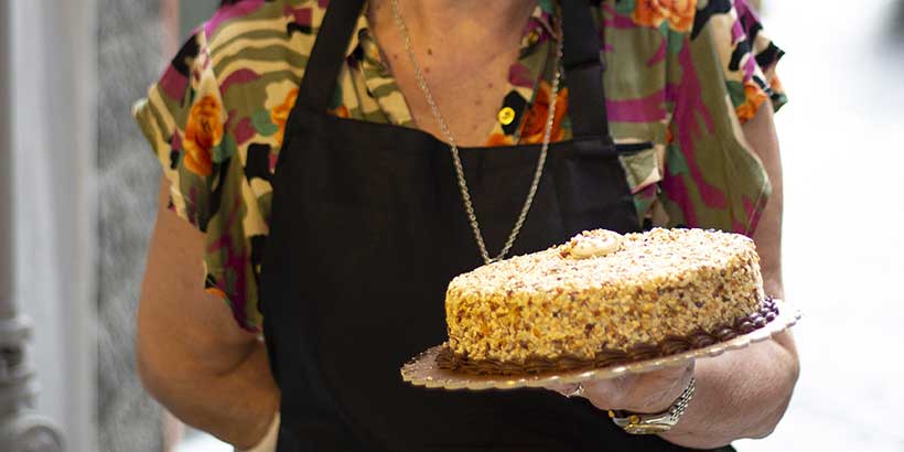Pâtissière à Naples tenant un gâteau artisanal aux amandes et sucre glace, spécialité de pâtisserie italienne.