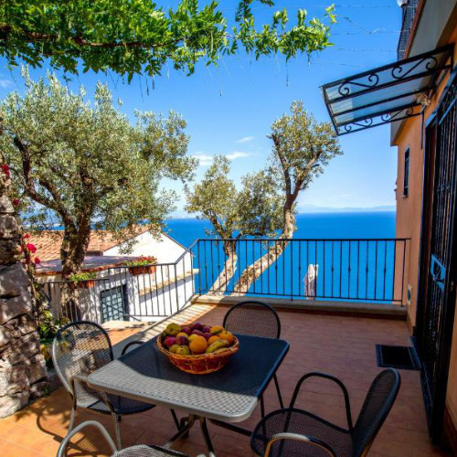 Terrasse ensoleillée à Il Glicine avec oliviers, corbeille de fruits et vue sur la mer.