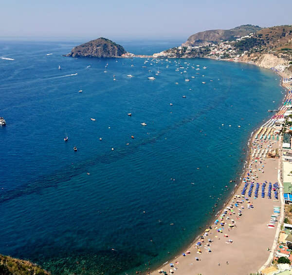 Vue aérienne de la plage des Maronti sur l'île d'Ischia, avec ses nombreux parasols colorés, les collines en terrasses et l'îlot Sant'Angelo en arrière-plan.