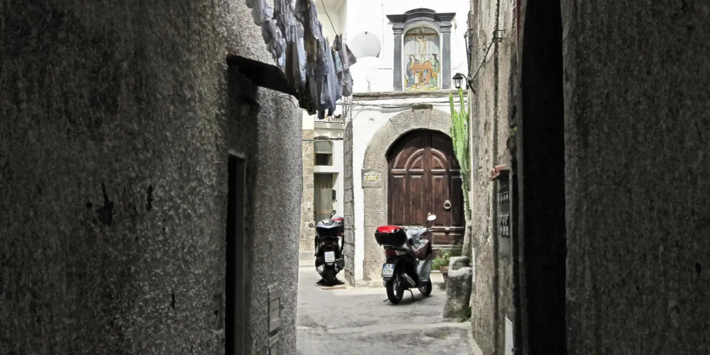 Ruelle typique d'Ischia avec du linge pendu aux fenêtres et des scooters garés.