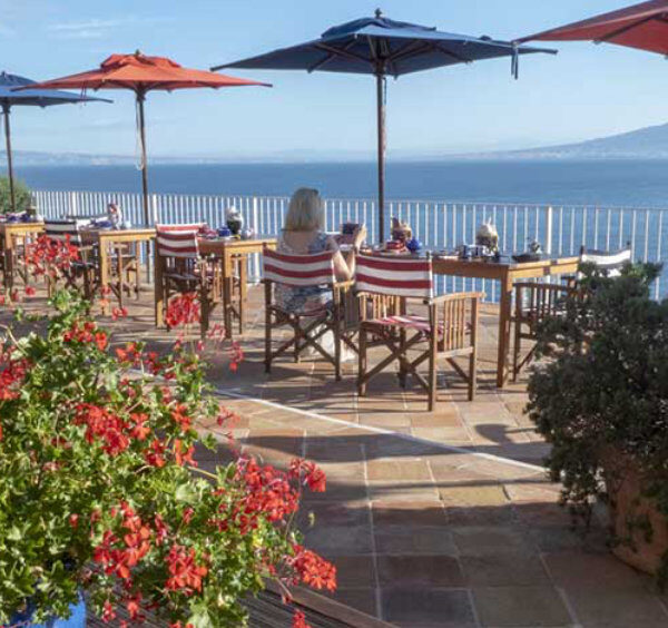 Terrasse panoramique à Sorrente avec tables, parasols et vue sur le Vésuve.