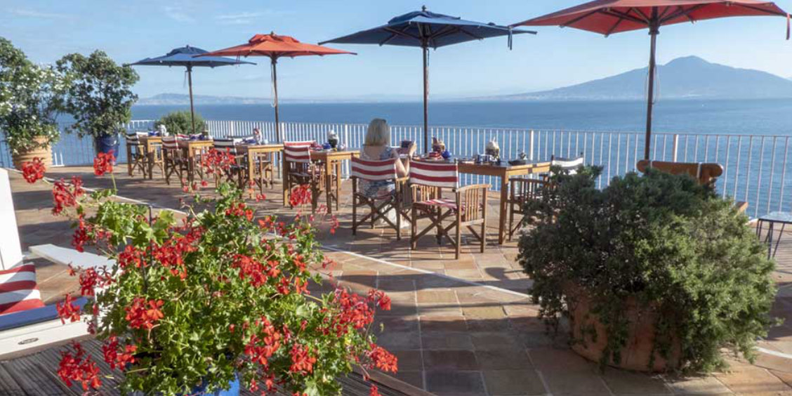 Terrasse panoramique à Sorrente avec tables, parasols et vue sur le Vésuve.