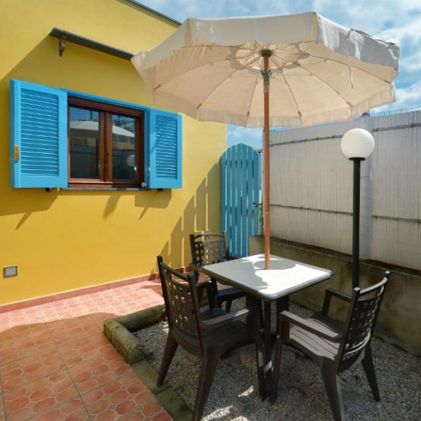 Patio extérieur privé aux murs jaunes et volets bleus, aménagé avec un salon de jardin et un parasol.