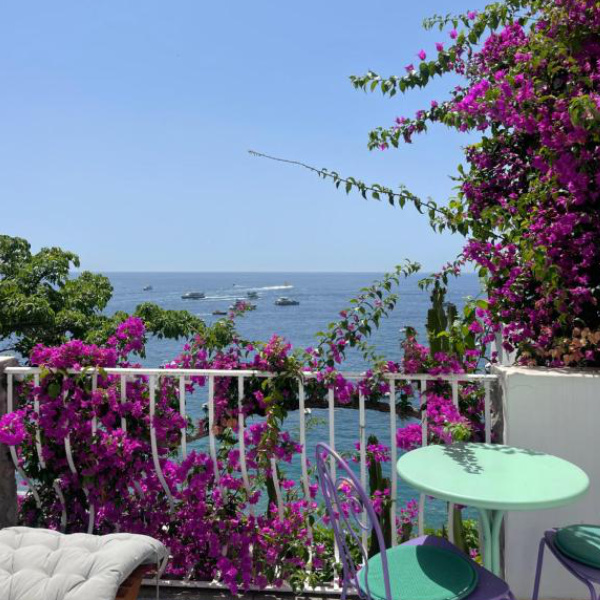 Balcon fleuri de La Dolce Vita à Positano avec table et vue panoramique sur la côte.