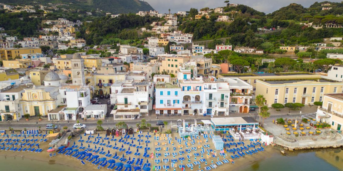 Vue panoramique de Lacco Ameno à Ischia avec sa plage de parasols colorés et son front de mer pittoresque.