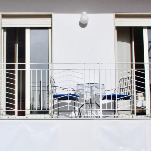 Balcon épuré avec une table et deux chaises bleues, offrant un espace de détente devant des baies vitrées.