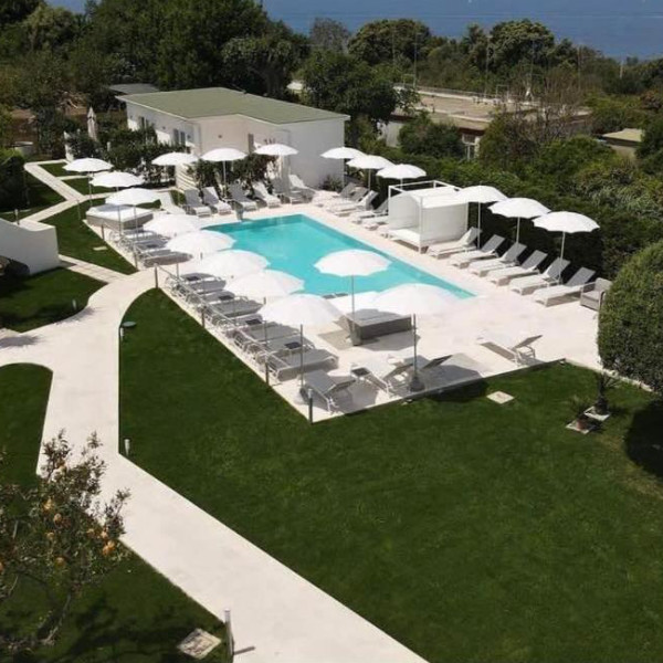 Vue aérienne de la piscine de l'établissement entourée de parasols blancs et d'une pelouse soignée.