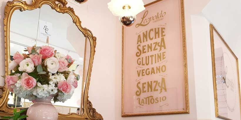 ntérieur élégant d’un café à Naples avec miroir décoratif, bouquet de fleurs et affiche indiquant options sans gluten et véganes.