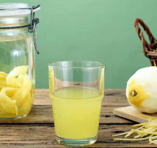 Préparation du limoncello avec citrons, zestes et verre de liqueur sur une table en bois.