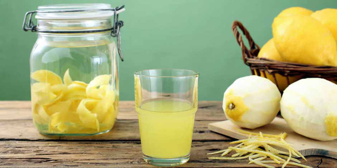 Préparation du limoncello avec citrons, zestes et verre de liqueur sur une table en bois.